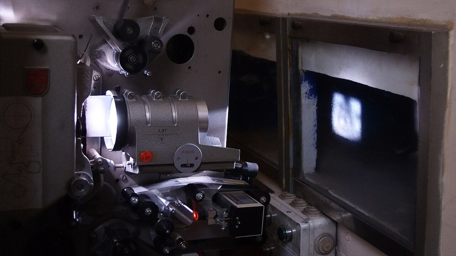 Close-up of a vintage film projector with a loaded reel in a dark theater booth, lit in magenta and gold