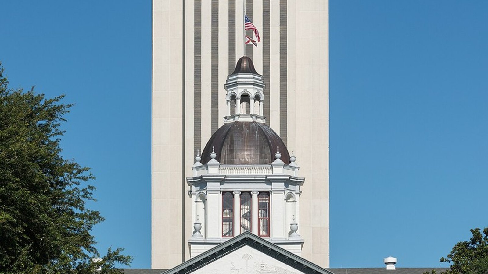 The Florida State Capitol in Tallahassee, a white tower behind the historic domed building under a deep blue sky