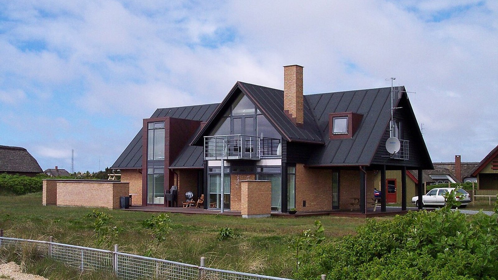 A suburban street of detached houses with slate roofs and sand-colored walls in clear daylight