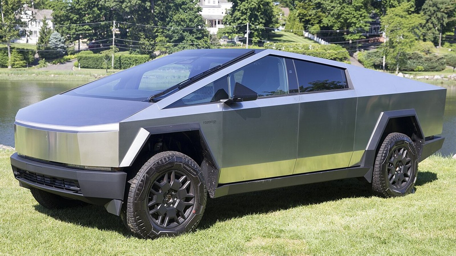 Close-up of a Tesla Cybertruck's stainless steel body panel and headlight against a dark navy background
