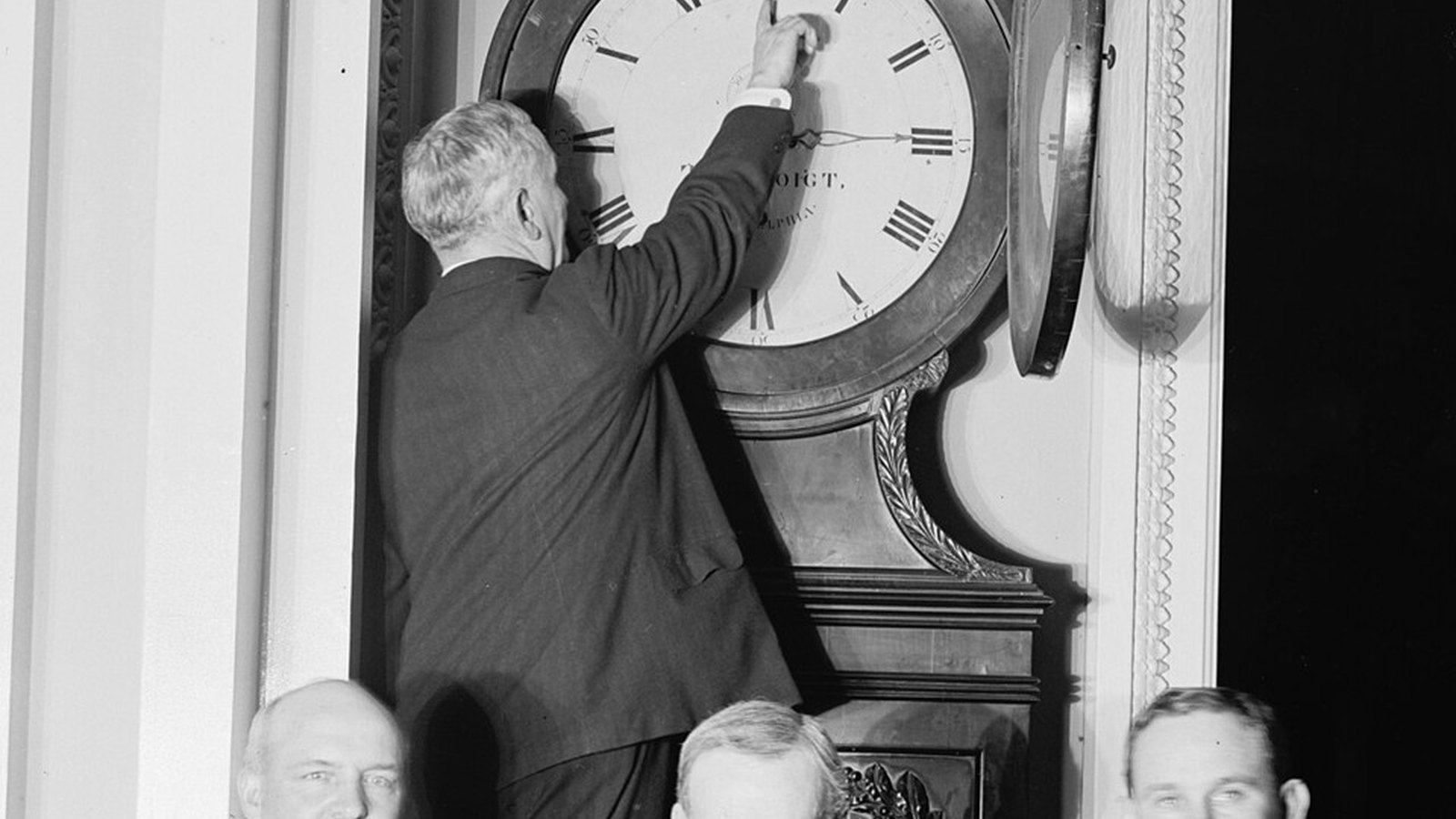 Blank-faced white wall clock beside a stack of paper with a red wax seal on a charcoal surface