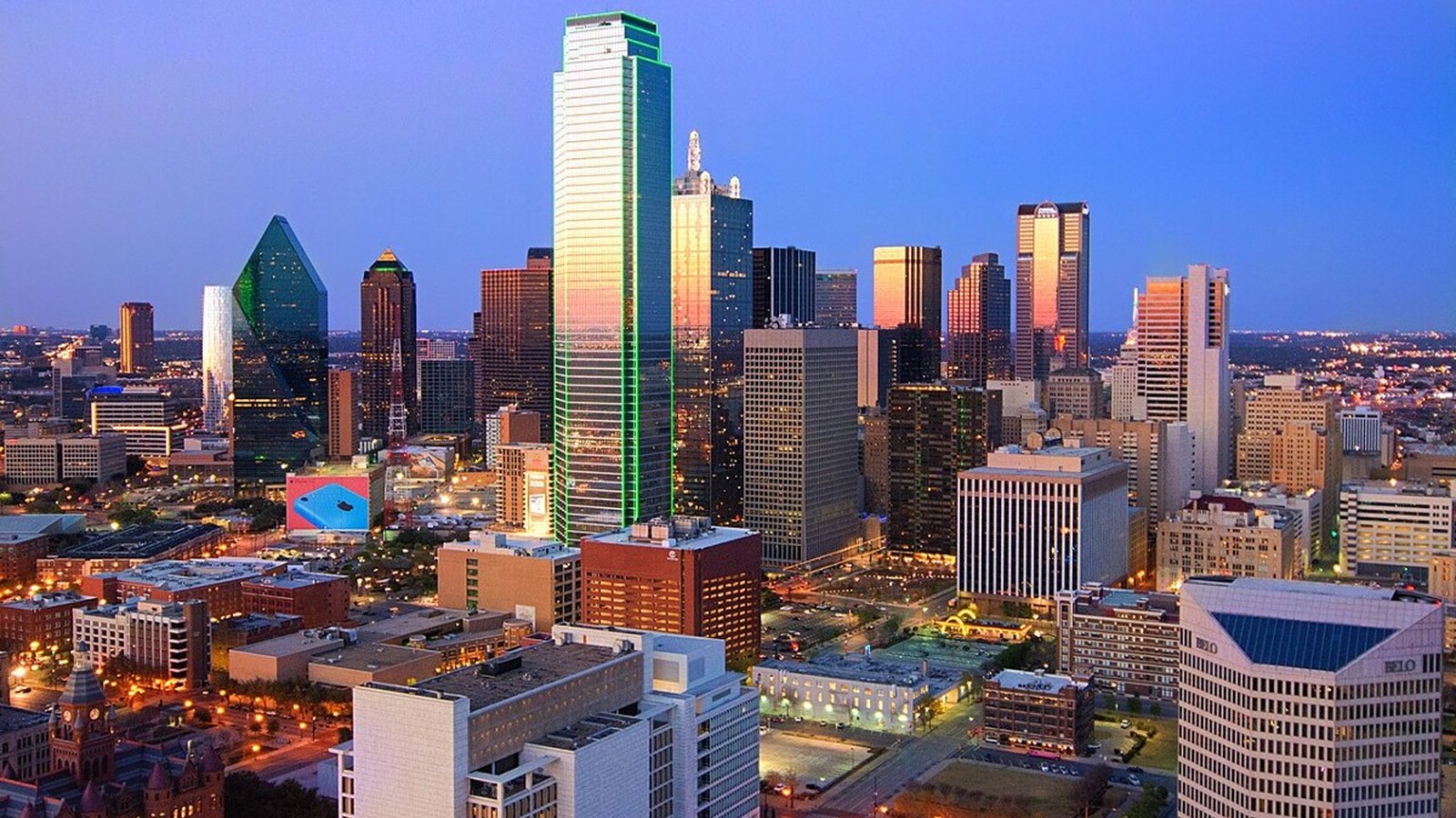Dark glass office towers of downtown Dallas rising under a clear daytime sky