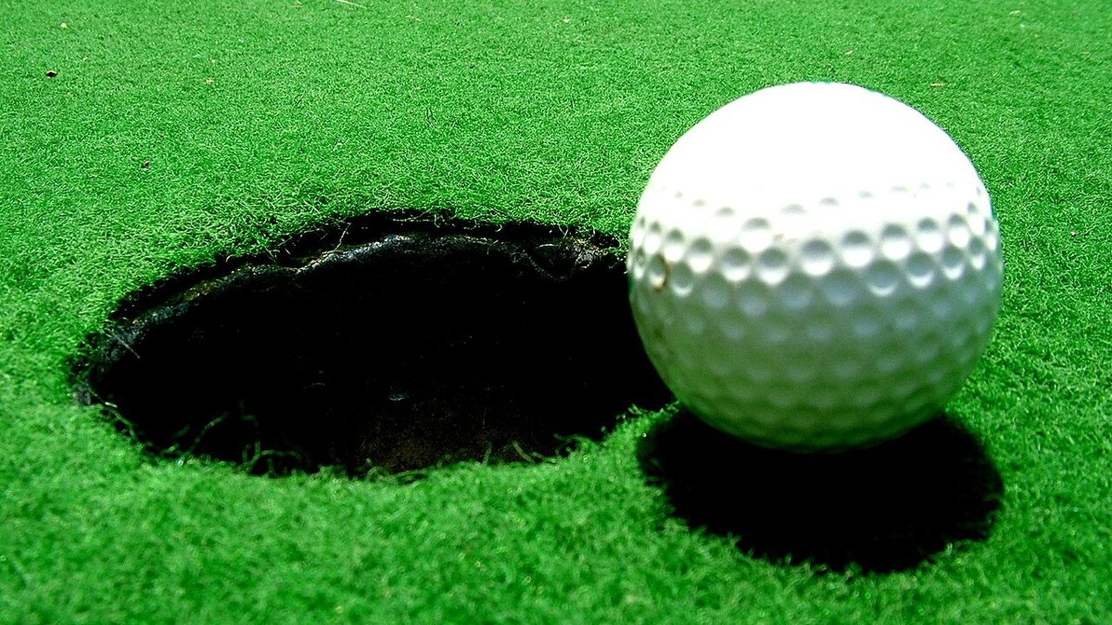A white golf ball on a raised green felt podium beside a small wooden token on a cream game board