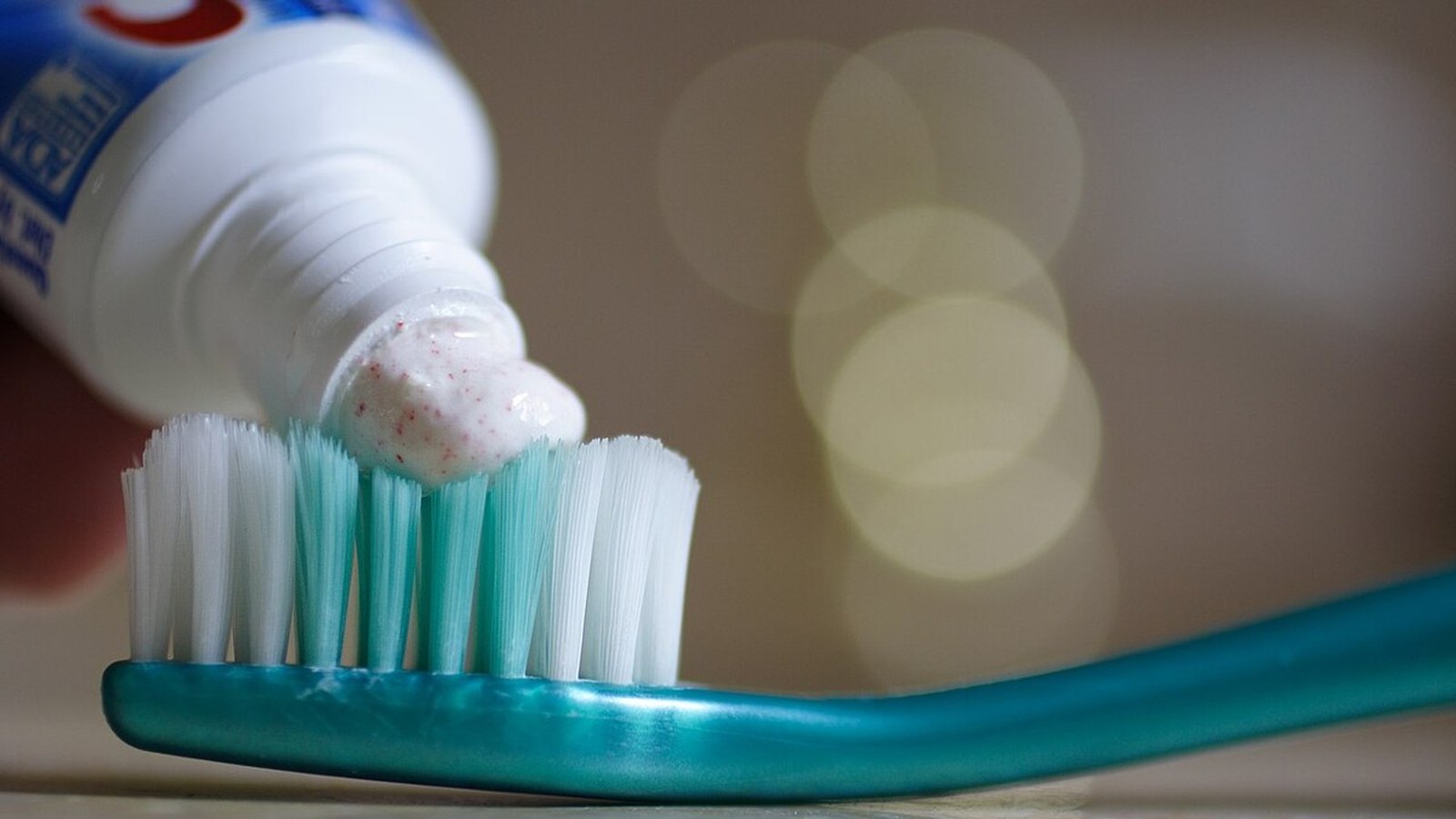 Row of blank chrome gray toothpaste tubes with red caps on a bathroom counter, one squeezed onto gray tile